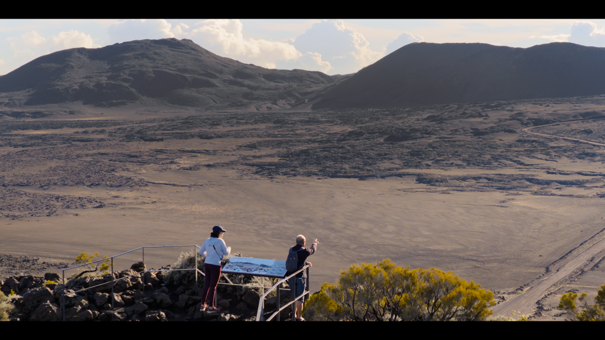 Vue panoramique de la Plaine des Sables à La Réunion, avec deux personnes observant le paysage volcanique depuis un belvédère.